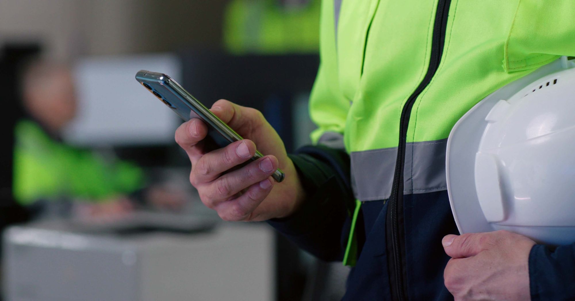 En person iført verneutstyr holder en smarttelefon. Foto.